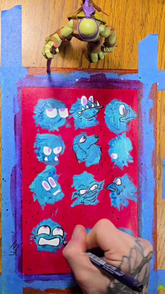 Nine fuzzy blue creatures painted on a crimson panel speckled with galaxy splatter, bordered with blue painter's tape.