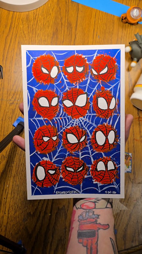 Twelve scratchy red masked hero heads with big white eyes painted across a blue web-patterned background.