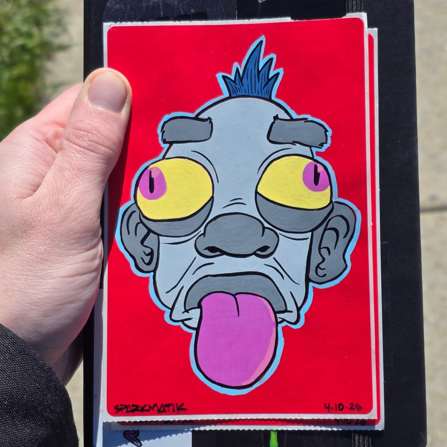 Magic the Gathering card fully painted over with a gray ghoul face, yellow eyes, blue mohawk and pink tongue sticking out, on a red background.
